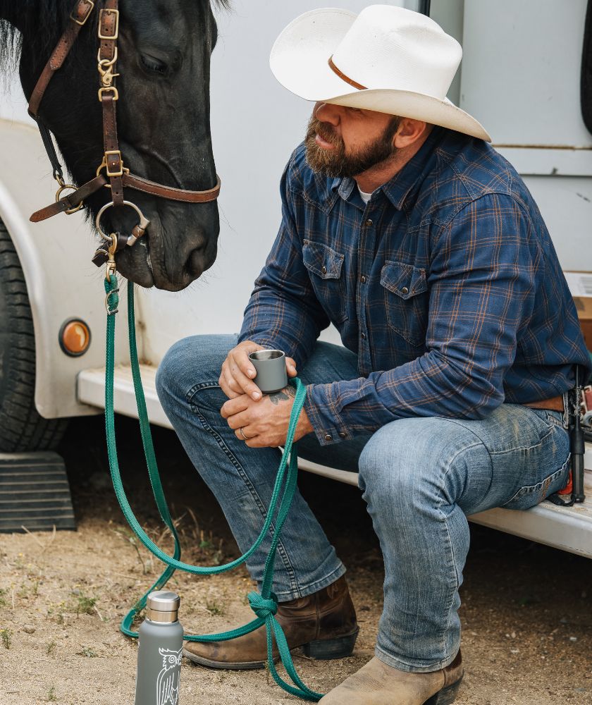 Cowboy sitting on step drinking coffee while holding horse lead